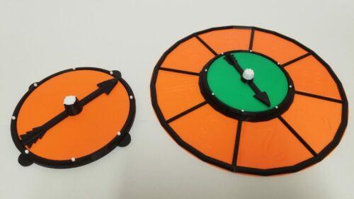 A picture of a game spinner with additional ring, and another game spinner in a larger size